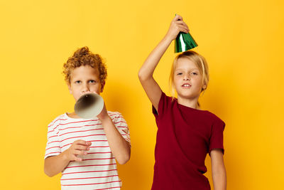 Portrait of happy friends holding mobile phone while standing against yellow background