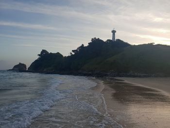 Lighthouse on beach by sea against sky during sunset