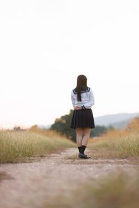 Rear view of woman walking on field against clear sky