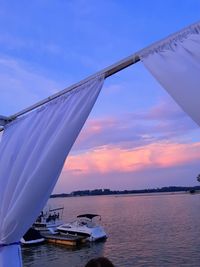 Sailboats moored on sea against sky during sunset