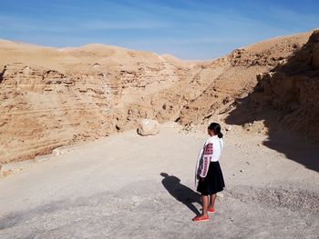 Rear view of woman standing by rock formation against sky