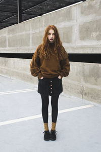 Full length portrait of young woman standing against wall