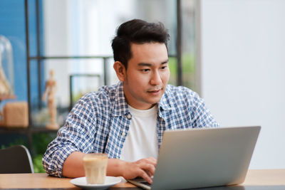 Portrait of young man using mobile phone while sitting on table