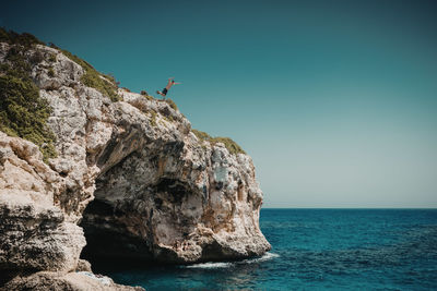 Rock formations by sea against clear sky