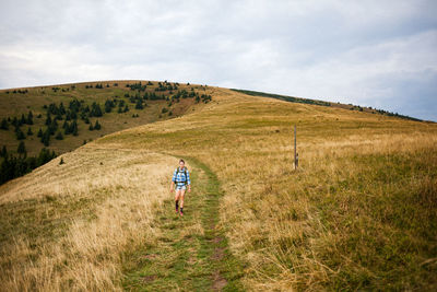 Rear view of man walking on field against sky