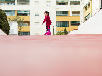 Little girl on bicycle looking at camera over shoulder while spending time with friends near modern apartment building