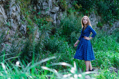 Young woman with hand on hip standing against rock formation in forest