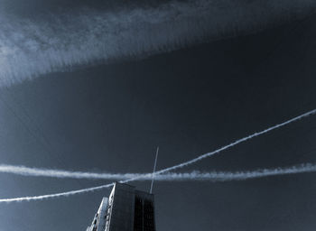 Low angle view of vapor trails over silhouette building against sky