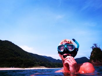 Close-up of young man snorkeling in sea against blue sky