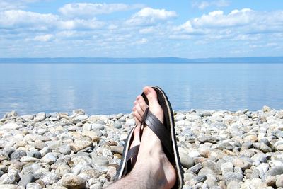 Person on rock at beach against sky