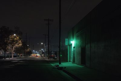 Empty road amidst illuminated buildings in city at night