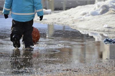 Low section of boy with basketball standing on puddle during winter