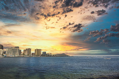 Sea and buildings against sky during sunset