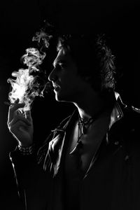 Portrait of man smoking cigarette against black background