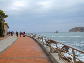 People on railing by sea against sky