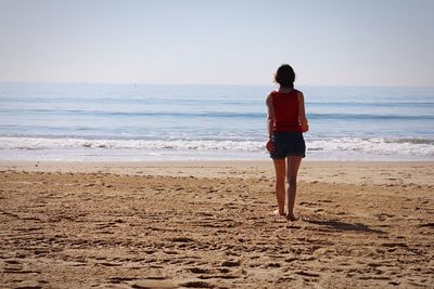 Rear view of woman standing at beach against sky