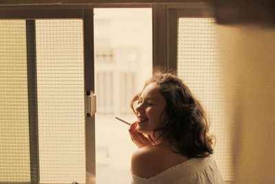 Smiling woman smoking cigarette by window