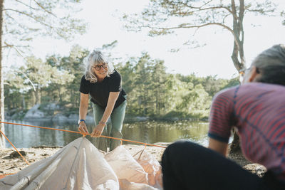 Two senior women setting up tent at campsite at lakeshore