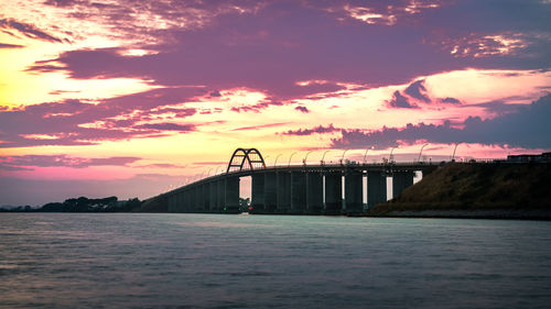 Silhouette bridge over sea against sky during sunset