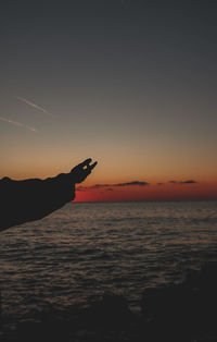 Silhouette hand by sea against sky during sunset