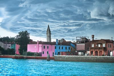 Houses at waterfront against cloudy sky