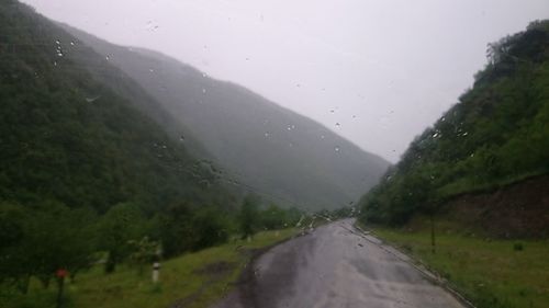 Wet road amidst trees during rainy season