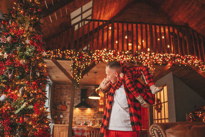 Candid authentic happy dad and son in red plaid pajamas fooling around at wood lodge xmas decorated