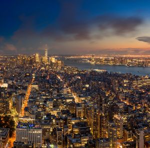 High angle view of illuminated cityscape by river against cloudy sky at dusk