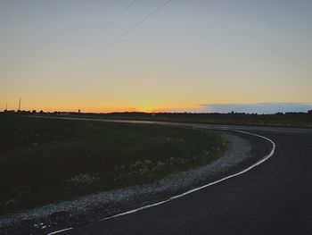 Road by silhouette field against clear sky at sunset