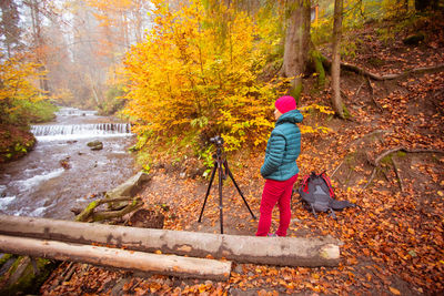 Full length of girl standing by stream in forest during autumn