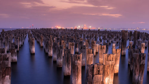 Panoramic view of wooden posts in sea against sky at sunset