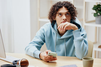 Thoughtful man holding phone sitting by desk