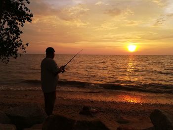 Rear view of a man fishing in sea at sunset