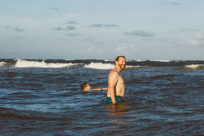 Father and son swimming in sea against sky