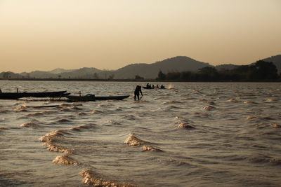 People in river against clear sky during sunset