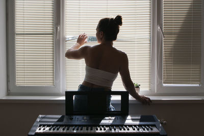 Young woman musician standing at the window. view from behind.