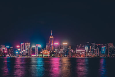 Illuminated buildings by river against sky at night