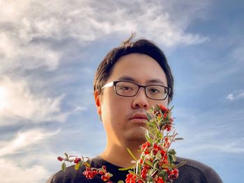 Portrait of young man with orange rowan berry branches against cloudy blue sky.