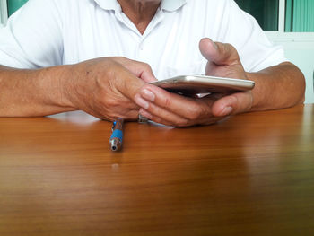 Midsection of man holding mobile phone while sitting on table
