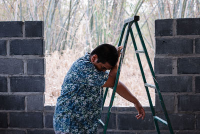Side view of young man standing against ladder