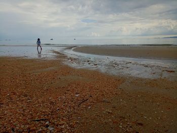 Girl walking at on shore at beach against sky