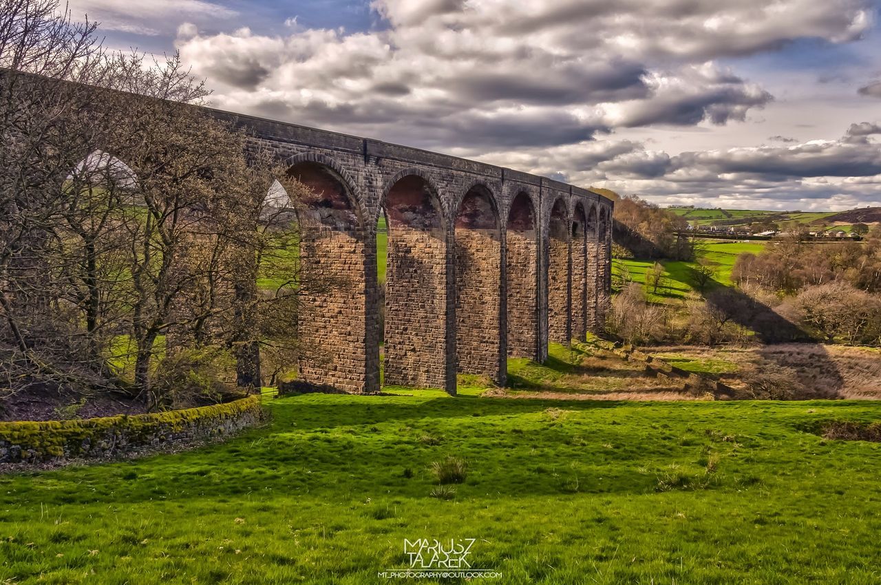 sky, architecture, built structure, grass, cloud - sky, history, cloudy, landscape, building exterior, old ruin, green color, stone wall, cloud, tranquility, old, arch, the past, mountain, field, nature