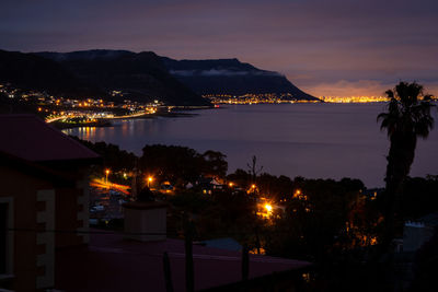 Illuminated city by sea against sky at night