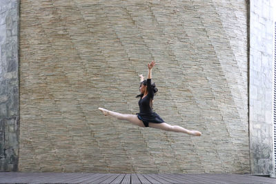 Full length of ballet dancer with legs apart jumping against wall