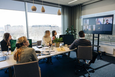 Male and female business colleagues looking at tv screen with video conference display in coworking office