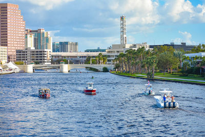 Boats in river by buildings in city against sky