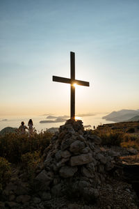 Cross on rock against sky at sunset