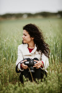 Beautiful woman with camera sitting on field