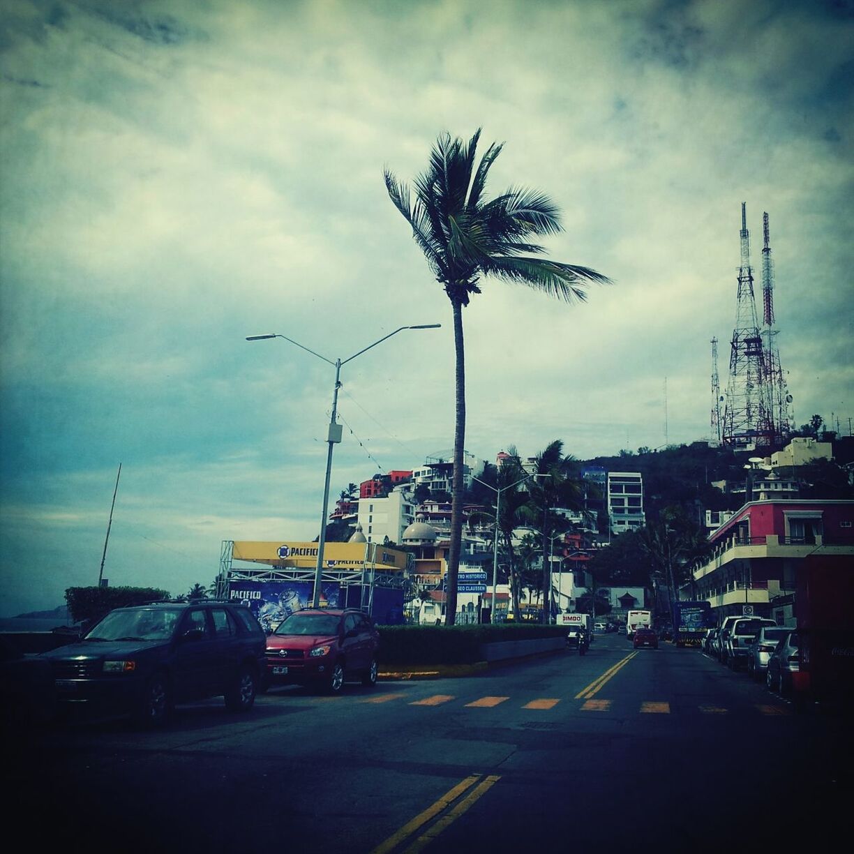 sky, transportation, car, building exterior, cloud - sky, street, road, built structure, architecture, land vehicle, mode of transport, cloudy, street light, cloud, palm tree, outdoors, city, the way forward, no people, road marking