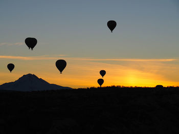 Silhouette hot air balloons flying in sky during sunset